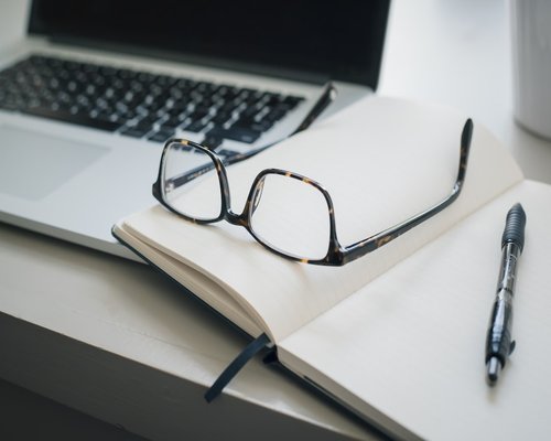 Detail of a desk with an open notebook, pen and glasses